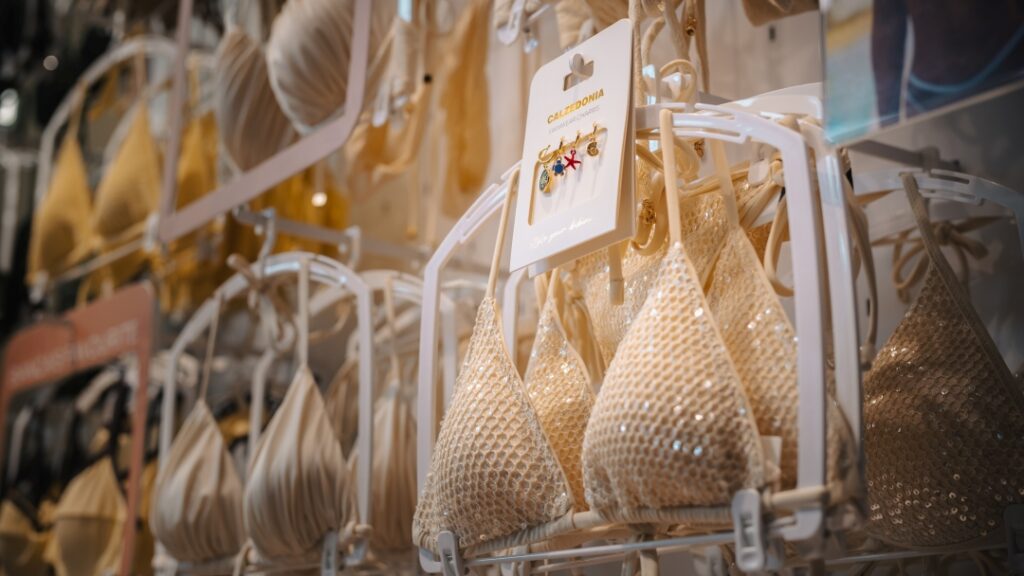 Bikinis, badkläder och strandaccessoarer upphängda på ställ i modebutik.