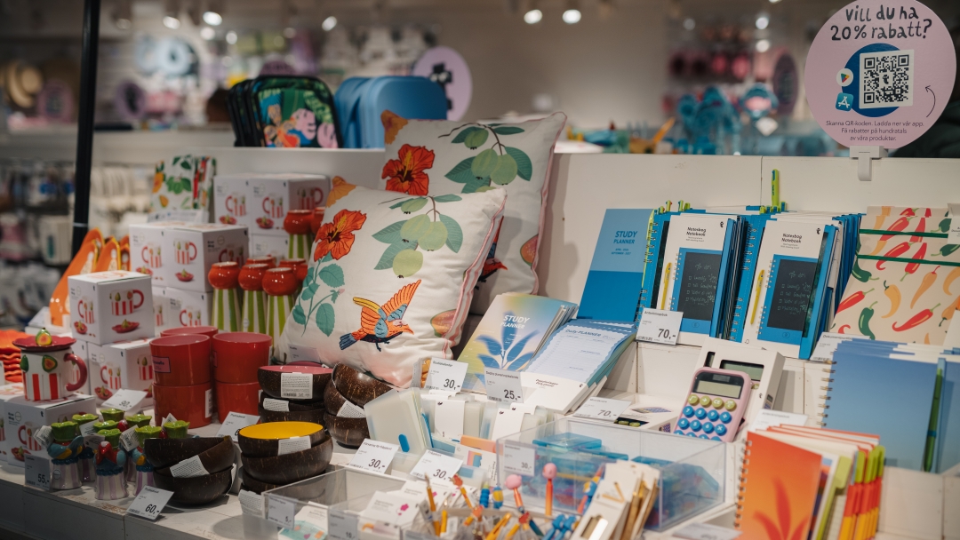 Butiksdisplay med färgglada anteckningsblock, köksartiklar, prydnadskuddar och presentprodukter.