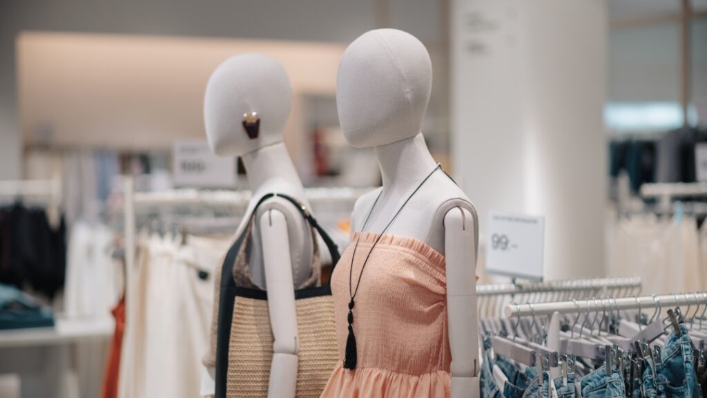 Skyltdockor i klädbutik visar sommarplagg och accessoarer intill klädställningar.