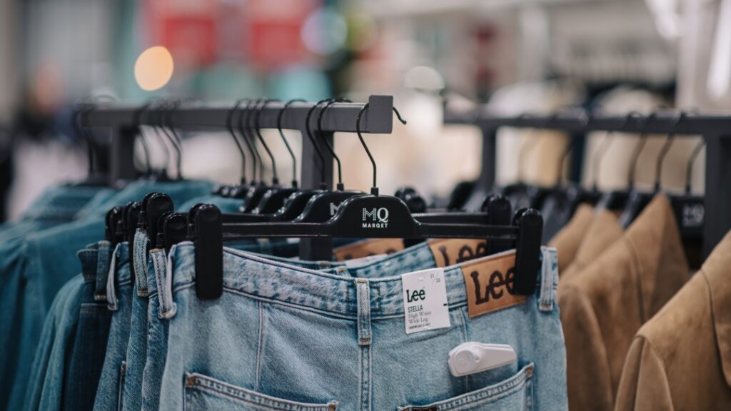 Jeans och ytterplagg upphängda på klädställningar i modebutik med fokus på denim.