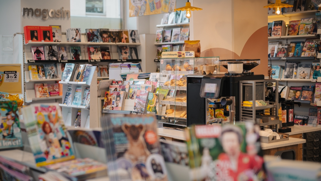 Tidnings- och servicebutik med magasin, böcker, kaffe och bakverk vid försäljningsdisk.