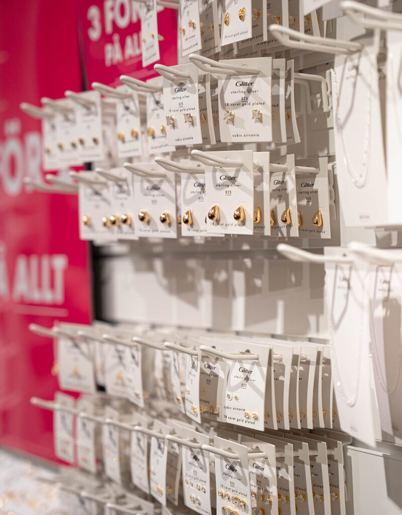 Display med guld- och silverörhängen i smyckesbutik, upphängda på vita produktkort med kampanjskylt i bakgrunden