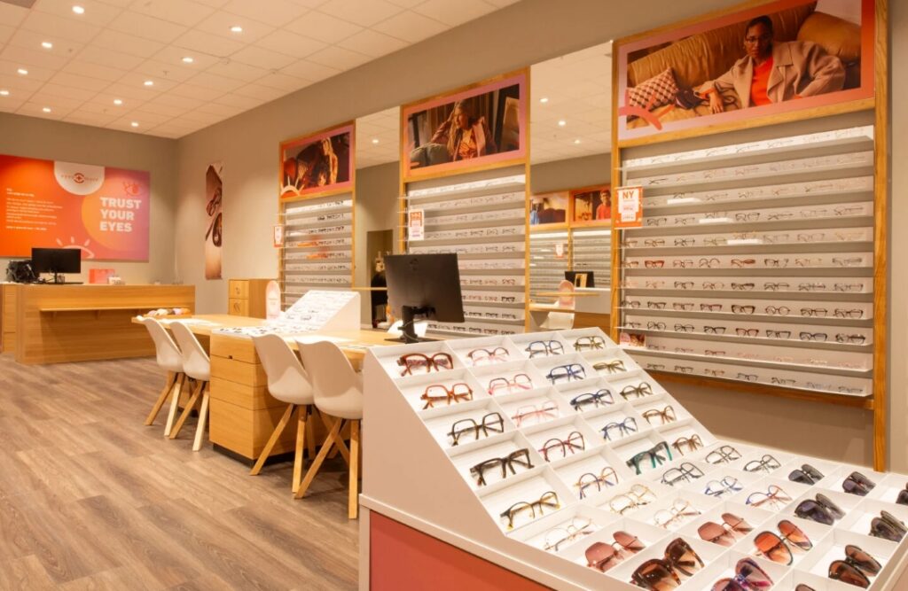 Optikerbutik med glasögonbågar på display och väggmonterade hyllor för synhjälpmedel.